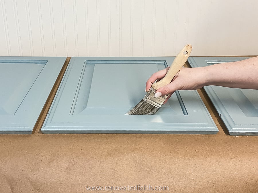 woman's hand painting on blue cabinet paint