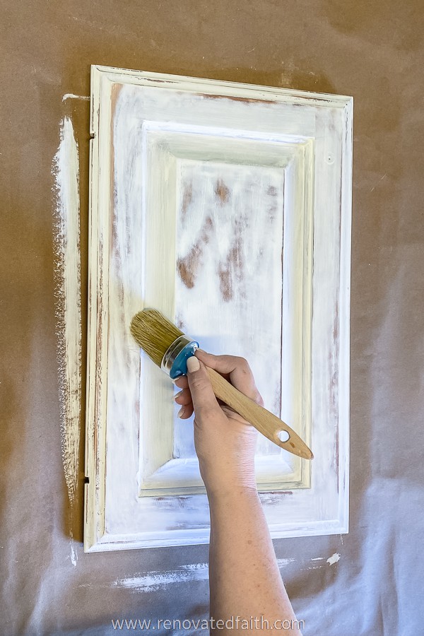 hand with chalk paint brush removing sanding dust from cabinet door